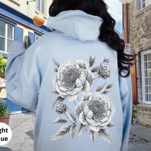 K&ouml;nnte beinhalten: Hellblauer Kapuzenpullover mit einem schwarz-wei&szlig;en Blumendesign aus Pfingstrosen und Bl&auml;ttern auf dem R&uuml;cken. Der Text "Light Blue" ist unten links zu sehen. Ein l&auml;ssiges, bequemes Kleidungsst&uuml;ck.