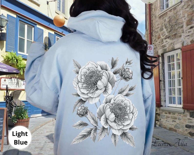 K&ouml;nnte beinhalten: Hellblauer Kapuzenpullover mit einem schwarz-wei&szlig;en Blumendesign aus Pfingstrosen und Bl&auml;ttern auf dem R&uuml;cken. Der Text "Light Blue" ist unten links zu sehen. Ein l&auml;ssiges, bequemes Kleidungsst&uuml;ck.