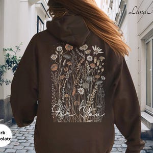 May include: Dark chocolate-colored hoodie with a floral design on the back. The design features various flowers and foliage in neutral tones, with the words "For You" in a cursive font. The hoodie has a hood and a relaxed fit.