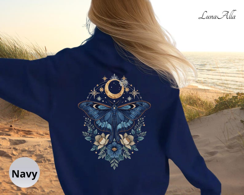 May include: A navy blue long-sleeve sweatshirt featuring a large back graphic of a moth centered beneath a crescent moon, surrounded by stars and floral elements. The text "Luna Alla" is printed in the upper right corner of the garment.