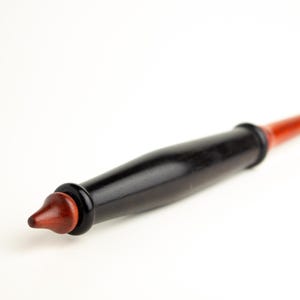 May include: A handcrafted wooden wand with a black handle and a reddish-brown tip. The wand has a smooth, polished finish and a simple, elegant design. The wand is a magical item.