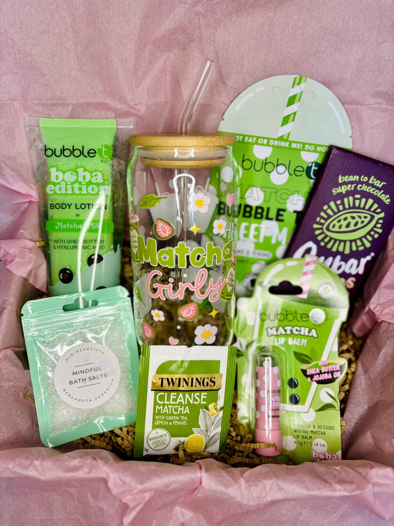 May include: A gift box filled with matcha-themed products. Includes a glass tumbler with a bamboo lid, lip balm, body lotion, bath salts, tea, and a chocolate bar. The tumbler has the words "Matcha Girly" and strawberry and flower designs.