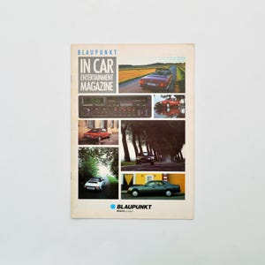 Puede incluir: Una portada de revista vintage con el texto "BLAUPUNKT IN CAR ENTERTAINMENT MAGAZINE". La portada incluye imágenes de coches clásicos, una radio de coche y vistas panorámicas de carreteras. El logotipo de Blaupunkt está en la parte inferior.
