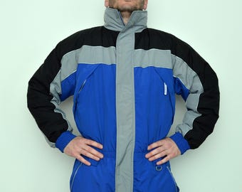 May include: A blue, black, and gray snowsuit. The snowsuit has a high collar, a zipper down the front, and blue cuffs. The sleeves are black with gray accents. The body of the snowsuit is blue with gray accents. The snowsuit is designed for cold weather.