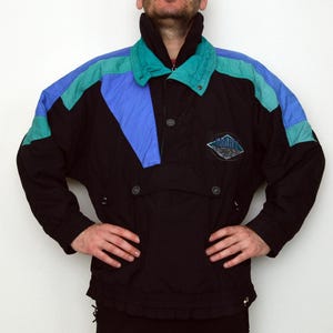 May include: Black and teal vintage ski jacket with blue and teal color block accents. The jacket features a high collar, a front pocket, and a logo patch on the chest. The jacket has a relaxed fit and is made of a durable, water-resistant material.