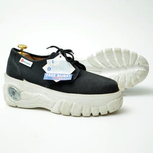 Può includere: Scarpe con plateau in tela nera con suole bianche. Le scarpe hanno lacci e un'etichetta con la scritta "FREE BURST". Le suole sono spesse e hanno un design strutturato. Su sfondo bianco.