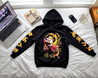 以下が含まれることがあります： 黒色のフード付きスウェットシャツ。前面にはカラフルなアニメのグラフィック、袖には日本語のテキストがプリントされています。炎に包まれたキャラクターが描かれています。白いベッドの上に置かれ、ノートパソコンと新聞が近くにあります。