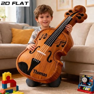 May include: A large, plush violin toy in shades of brown, with black strings and musical notes. The toy has the name "Thomas" printed on it. The image also shows a child holding the toy, and other toys in the background.