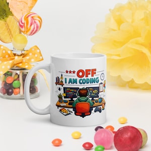 Pode incluir: Caneca de cerâmica branca com uma ilustração colorida de uma pessoa codificando em uma mesa, com o texto "OFF I AM CODING". O design inclui um computador, pizza e um controle. A caneca é cercada por doces.