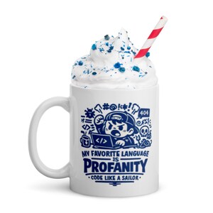 May include: White coffee mug with a blue cartoon graphic of a person coding on a laptop, with the text "MY FAVORITE LANGUAGE IS PROFANITY - CODE LIKE A SAILOR." The mug is topped with whipped cream, blue sprinkles, and a red and white striped straw.