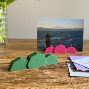 Op de afbeelding: Op een houten tafel staan een boeket tulpen in een glazen vaas, een ansichtkaart met een berglandschap en groene geometrische vormen. Er ligt ook een stapel wenskaarten met het woord "THANKS".