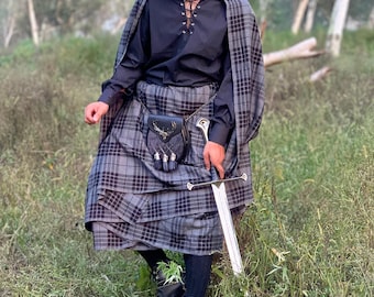 May include: A traditional Scottish outfit featuring a gray and black plaid kilt, matching cape, and a black shirt with a lace-up front. The ensemble includes a black beret, sporran, and a silver sword. The outfit is completed with black boots.