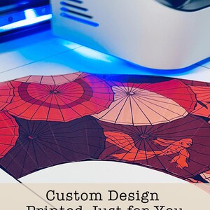 Może przedstawiać: Niestandardowy wachlarz z powtarzającym się wzorem czerwonych, pomarańczowych i białych parasoli. Widoczny jest tekst "Custom Design Printed Just for You". Wachlarz jest drukowany przez maszynę.