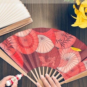 Może przedstawiać: Ręcznie robione wachlarze z czerwonym wzorem parasoli. Tekst na zdjęciu brzmi "HANDCRAFTED FANS Handmade in our California garage 30 minutes total". Wachlarz jest wykonany z drewna i papieru.