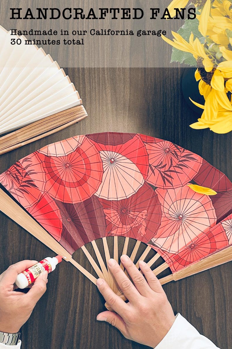 Może przedstawiać: Ręcznie robione wachlarze z czerwonym wzorem parasoli. Tekst na zdjęciu brzmi "HANDCRAFTED FANS Handmade in our California garage 30 minutes total". Wachlarz jest wykonany z drewna i papieru.