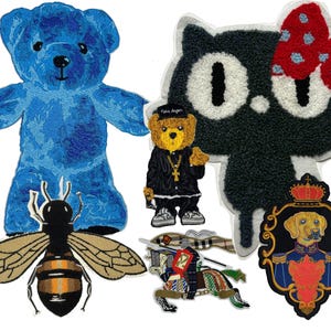 May include: A collection of six embroidered patches featuring a blue teddy bear, a black cat with a red polka dot bow, a small bear in a black outfit, a bee with tan wings, a knight on horseback, and a dog in a royal uniform with a crown.