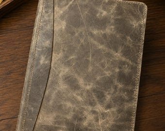 May include: A rectangular notebook cover in a distressed, weathered gray-brown finish. The cover features a vertical stitched panel along the left side, with visible tonal stitching along all edges and a textured, marbled surface appearance.