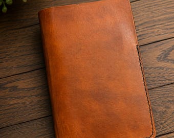 May include: A rectangular, tan-colored leather notebook cover with a smooth, slightly distressed finish. The cover features visible dark stitching along the edges, providing a clean, structured border for the folded leather construction.