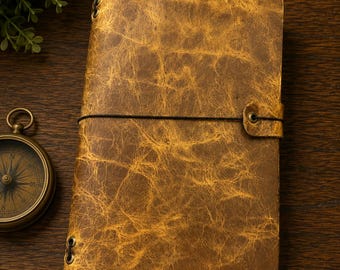 May include: A rectangular notebook with a distressed, textured tan and brown leather cover. The notebook is secured by a thin black elastic cord that wraps around the center and attaches to a small tab on the right side with a metal eyelet.