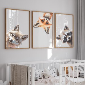 Puede incluir: Tres láminas enmarcadas con ilustraciones de animales: un zorro, un mapache y un lobo. Las ilustraciones en acuarela tienen una paleta de colores neutros y se exhiben sobre una cuna blanca con almohadas decorativas y una manta.