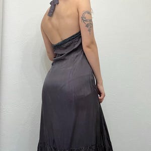 May include: A dark gray halter dress with a flowing silhouette. The dress features a low back and a decorative trim along the neckline. The hemline has a darker, textured pattern.