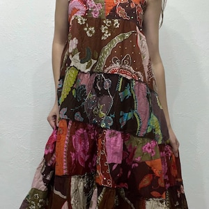 以下が含まれることがあります： 茶色、オレンジ、ピンク、緑の花柄のパッチワークマキシドレス。 ドレスは細いストラップとティアードスカートが特徴です。 生地は薄手で、暖かい季節に適しているようです。