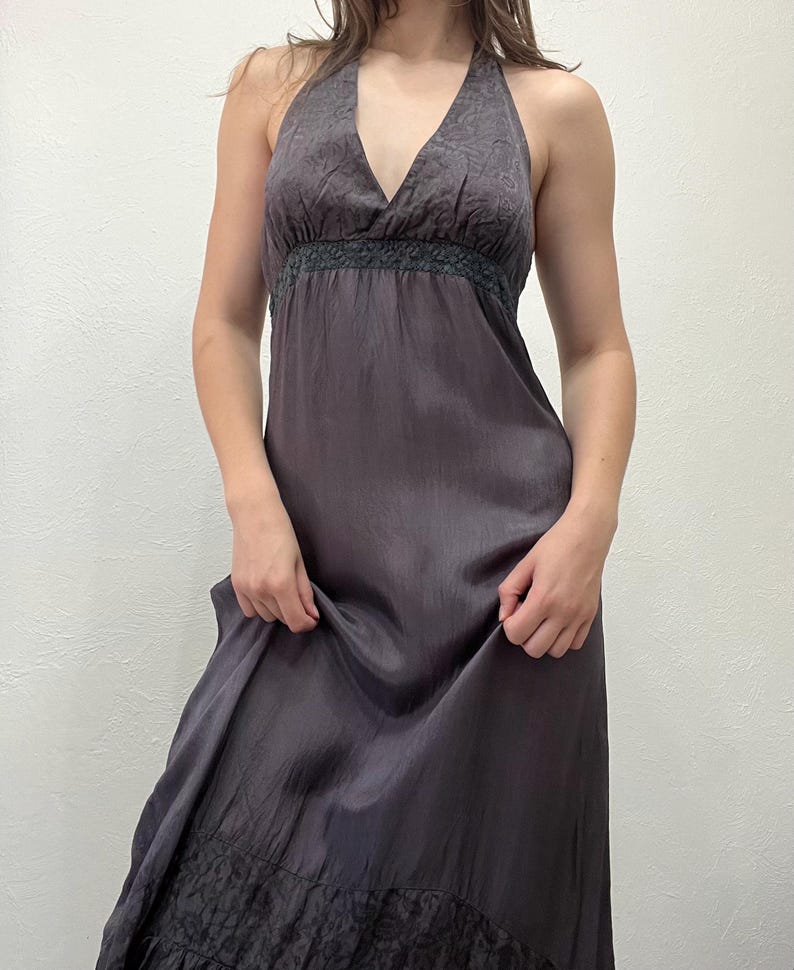 May include: A dark gray halter dress with a V-neckline and a flowing skirt. The dress features a textured pattern on the bodice and a ruffled hem. The fabric has a subtle sheen, giving it a luxurious appearance.