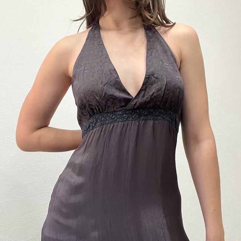 May include: A dark grey halter top dress with a V-neckline. The dress has a textured fabric and a black lace detail at the waist. The dress is made of a silky material.