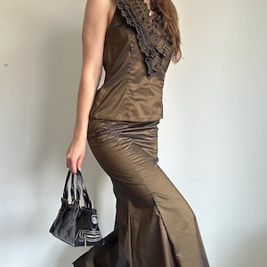 Bronze satin skirt set with a sleeveless ruffle top and long mermaid-style skirt, styled with a black handbag. A Y2K evening glam outfit with a sleek metallic shine for party or special occasion wear.