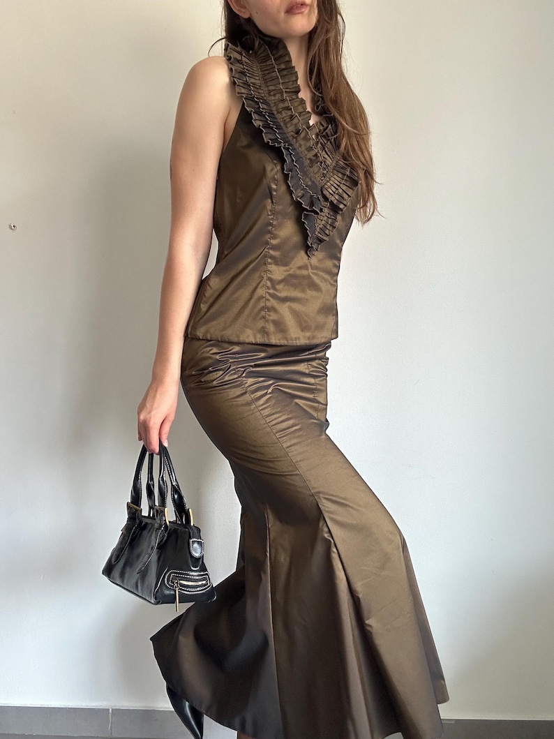 Bronze satin skirt set with a sleeveless ruffle top and long mermaid-style skirt, styled with a black handbag. A Y2K evening glam outfit with a sleek metallic shine for party or special occasion wear.