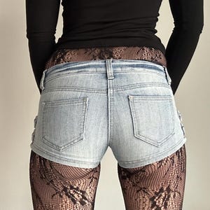 Könnte beinhalten: Hellblaue Jeansshorts mit Gesäßtaschen und Seitendetails. Die Shorts werden mit schwarzen Spitzentights und einem schwarzen Langarm-Oberteil kombiniert. Ein einfaches, stilvolles Outfit.