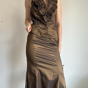 May include: A two-piece formal outfit in a bronze color. The top is a halter-style with a ruffled collar. The skirt is a floor-length, fitted design with a slight flare at the bottom. The fabric has a subtle sheen.