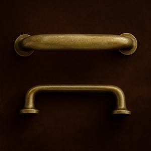 May include: Two antique brass cabinet pulls. The top pull is a horizontal bar with rounded ends. The bottom pull is a curved bar with circular mounting plates. Both have a textured finish and are set against a dark brown background.