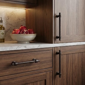 May include: A kitchen interior featuring dark wood cabinetry with black metal hardware. A bowl of pomegranates sits on a marble countertop, next to olive oil bottles. The cabinet doors have vertical handles, and the drawers have horizontal pulls.