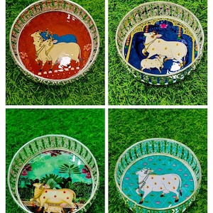 May include: Four decorative round trays with intricate silver filigree edges. Each tray features a different colorful painted scene of cows and calves. The backgrounds vary in shades of red, blue, green, and turquoise.
