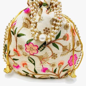Può includere: Una borsa a sacchetto color crema con chiusura a coulisse, caratterizzata da ricami floreali nei toni del rosa, arancione e verde. La borsa è decorata con paillettes dorate e un manico composto da più fili di perle bianche con una perla centrale.