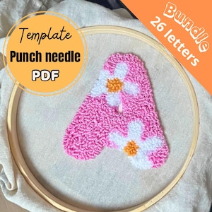 May include: A pink punch needle letter "A" with white and yellow flower accents, displayed in a wooden embroidery hoop. The image includes text that reads "Template Punch needle PDF" and "Bundle 26 letters".
