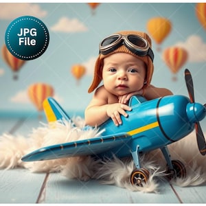 May include: A baby wearing a brown aviator hat and goggles, resting on a blue toy airplane with yellow accents. The airplane sits on a fluffy white surface, with hot air balloons in the background.