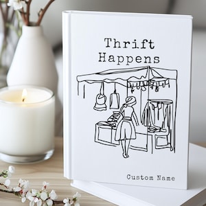 K&ouml;nnte beinhalten: Ein wei&szlig;es Notizbuch mit dem Text "Thrift Happens" und einer Schwarz-Wei&szlig;-Illustration einer Marktszene. Das Notizbuch hat auch die Worte "Custom Name" unten.