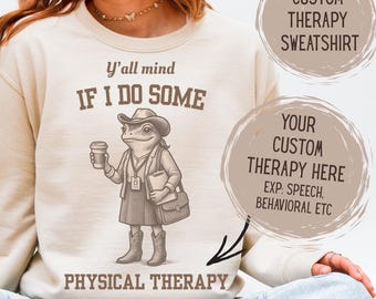 May include: Cream-coloured sweatshirt featuring a cartoon frog in a therapist outfit, holding a coffee cup and notepad. The text on the sweatshirt says "Y'all mind if I do some PHYSICAL THERAPY." Additional text reads "CUSTOM THERAPY SWEATSHIRT" and "YOUR CUSTOM THERAPY HERE".