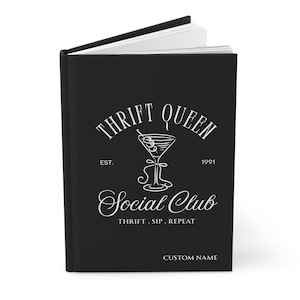 K&ouml;nnte beinhalten: Schwarzes Notizbuch mit dem wei&szlig;en Schriftzug "THRIFT QUEEN Social Club". Das Design beinhaltet eine Cocktailglas-Illustration und die Worte "THRIFT. SIP. REPEAT." Das Notizbuch ist ge&ouml;ffnet und zeigt wei&szlig;e Seiten.