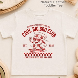 May include: A natural heather toddler t-shirt featuring a red graphic of a pizza slice on a skateboard. The text reads: OFFICIALLY PROMOTED TO THE COOL BIG BRO CLUB, EST. 2027, and CRUISING INTO BIG BRO LIFE, with a red and white checkered pattern.