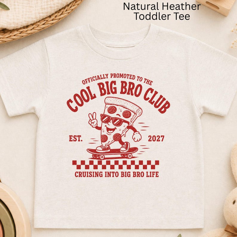May include: A natural heather toddler t-shirt featuring a red graphic of a pizza slice on a skateboard. The text reads: OFFICIALLY PROMOTED TO THE COOL BIG BRO CLUB, EST. 2027, and CRUISING INTO BIG BRO LIFE, with a red and white checkered pattern.
