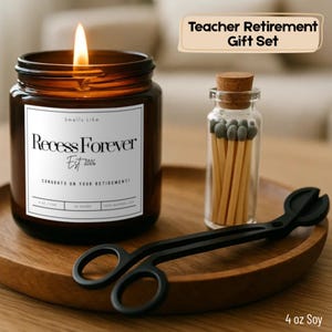 May include: A Teacher Retirement Gift Set includes a lit candle in a brown jar with the text "Recess Forever Est 2026", a small glass jar of matches, and black wick trimmers. The candle is 4 oz.