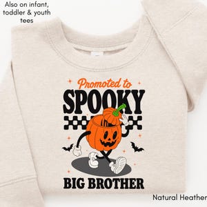 May include: A natural heather crewneck sweatshirt featuring a graphic of a cartoon pumpkin character with a jack-o'-lantern face, wearing shoes and gloves. The text reads Promoted to SPOOKY BIG BROTHER, accented by black bats, stars, and a checkered pattern.