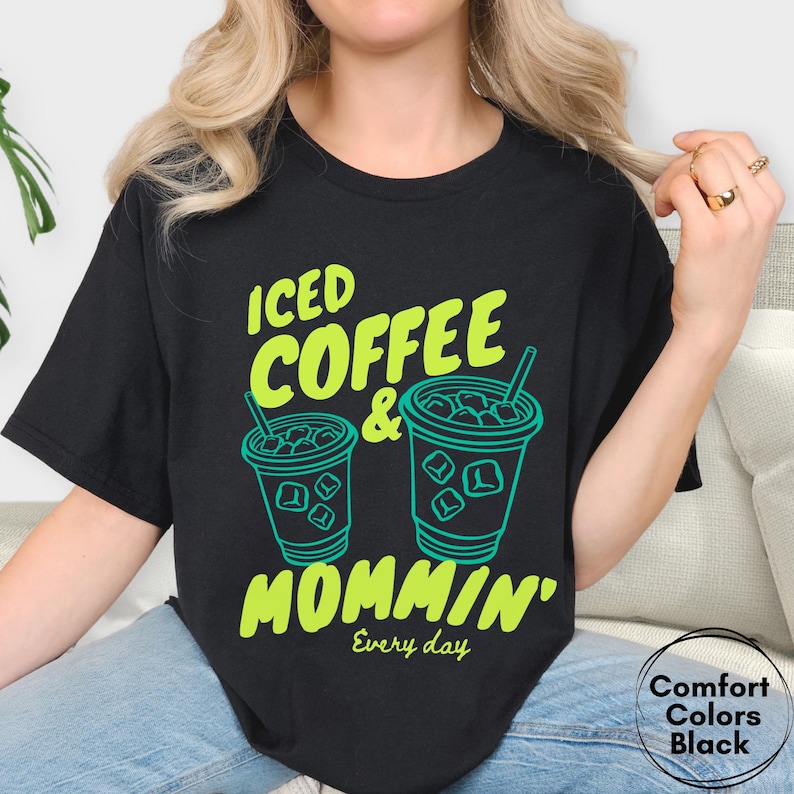 May include: Black t-shirt with the text "ICED COFFEE & MOMMIN' Every day" in neon green. Two iced coffee cup illustrations are also in neon green. The shirt is a Comfort Colors brand.