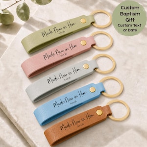 May include: Five leather keyrings in pastel shades: green, pink, grey, blue, and brown. Each keyring has a gold ring and a gold stud. The text "Made New in Him 8.13.26" is printed on each keyring. A custom baptism gift.