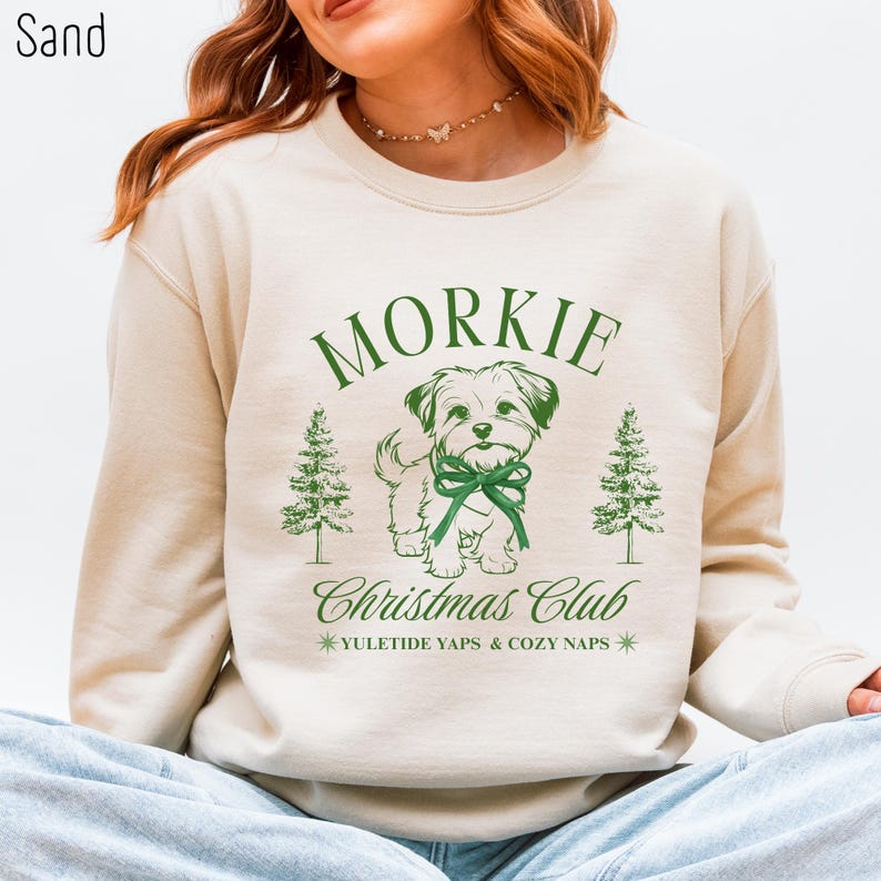 May include: Sand-colored sweatshirt with a green graphic of a Morkie dog wearing a bow, flanked by Christmas trees. Text reads "Morkie Christmas Club" and "Yuletide Yaps & Cozy Naps."