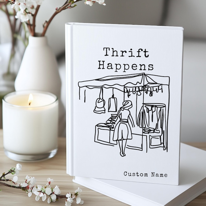 K&ouml;nnte beinhalten: Ein wei&szlig;es Notizbuch mit dem Text "Thrift Happens" und einer Schwarz-Wei&szlig;-Illustration einer Marktszene. Das Notizbuch hat auch die Worte "Custom Name" unten.