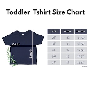 May include: A navy blue toddler t-shirt displayed next to a size chart titled Toddler Tshirt Size Chart. The chart lists sizes 2T through 7T with corresponding width and length measurements in inches, ranging from 12 to 16 inches wide and 15.50 to 19.50 inches long.